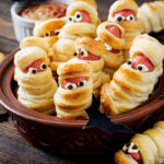 Scary sausage mummies in dough with funny eyes on table as halloween appetizers