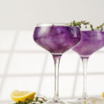 purple drink in a vintage glass for sparkling wine - pea flower tea or blue curacao sirup cocktail with thyme branches