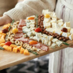 Woman holding an appetizer cheese board on background of stylish christmas table with fir branches and candles