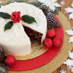 Christmas cake with white snowflake and red bauble decorations over oak background.