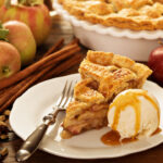 Piece of an apple cream pie with ice cream scoop and caramel sauce on a plate
