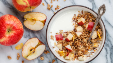Homemade granola (muesli) with oatmeal, nuts, flaxseed, cornflakes, fresh red apple, cinnamon and yogurt