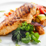 Macro shot of grilled chicken fillet with side dish of baked vegetables on white restaurant plate isolated.