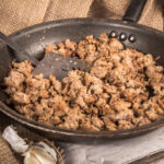 Cooking Ground sausage meat in frying pan with garlic and burlap