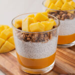 a mango dessert of shia seed pudding with fresh mango, granola in glass on light wooden table