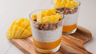 a mango dessert of shia seed pudding with fresh mango, granola in glass on light wooden table