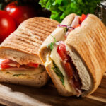 Toasted panini with ham, cheese and arugula sandwich on cutting board