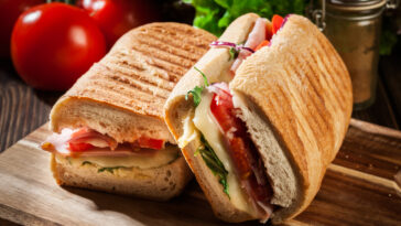 Toasted panini with ham, cheese and arugula sandwich on cutting board