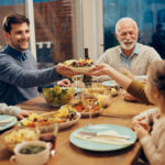 Happy couple passing food while having saturday night dinner in dining room.