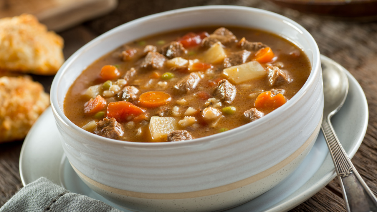 A bowl of delicious beef and barley soup with carrots, tomato, potato, celery, and peas.
