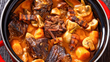 Beef Bourguignon, Beef Burgundy, stew with beef, bacon, carrots, onion bulbs and mushrooms in rich red wine sauce in pot on wooden table