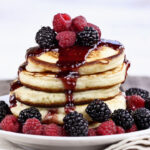 Delicious homemade golden pancakes with fresh blackberry, raspberries, and raspberry syrup.