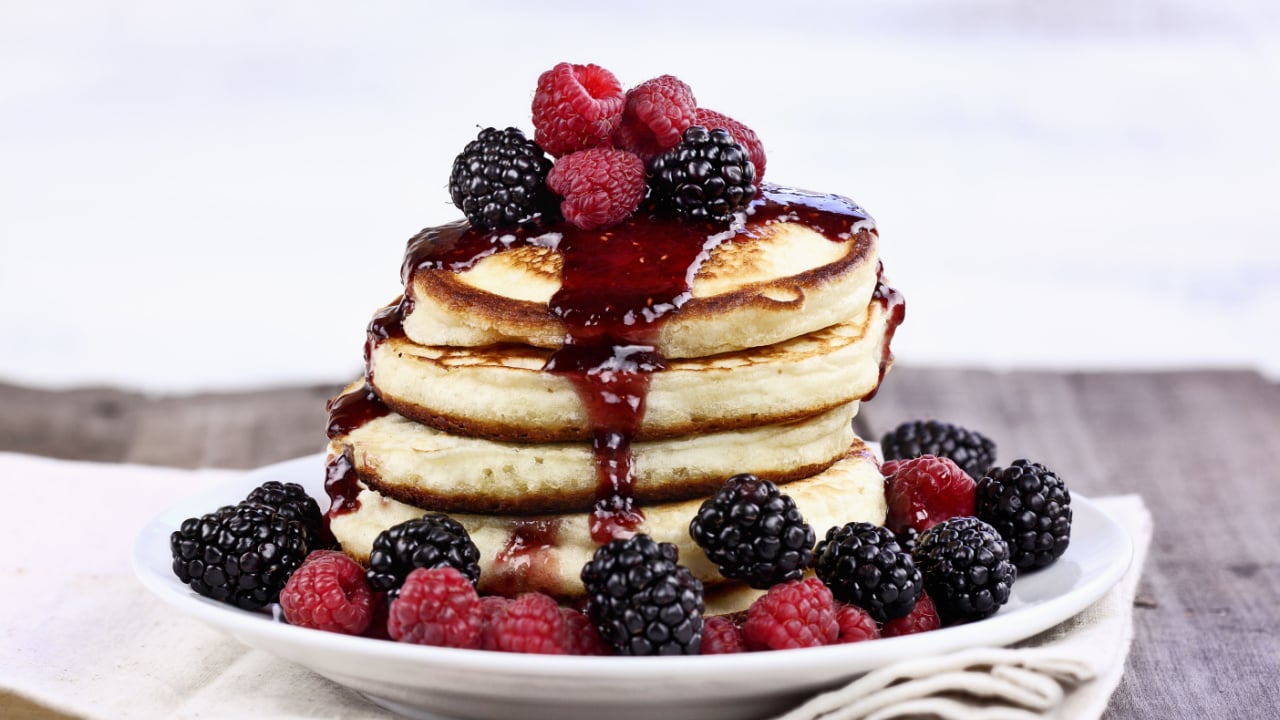 Delicious homemade golden pancakes with fresh blackberry, raspberries, and raspberry syrup.
