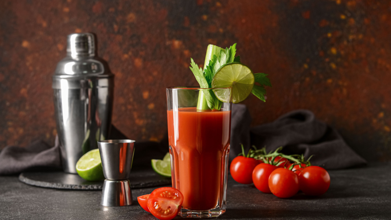 Glass of bloody mary with celery, lime and tomatoes on table
