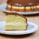 Piece of Boston cream pie in front with the whole pie in the background.
