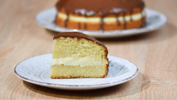 Piece of Boston cream pie in front with the whole pie in the background.