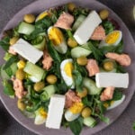 Salad with canned salmon, egg, cucumber, arugula and feta cheese on round plate.