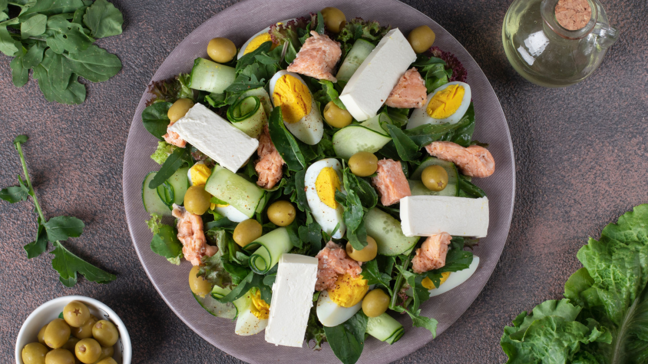 Salad with canned salmon, egg, cucumber, arugula and feta cheese on round plate.