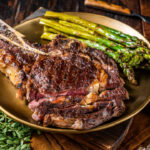 Sliced Grilled Cowboy or rib eye with bone beef steak, roasted asparagus in a plate. Wooden background.