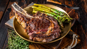 Sliced Grilled Cowboy or rib eye with bone beef steak, roasted asparagus in a plate. Wooden background.