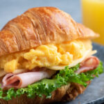 Croissant sandwich with turkey ham, scrambled eggs, cheese and lettuce salad.