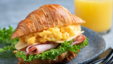 Croissant sandwich with turkey ham, scrambled eggs, cheese and lettuce salad.