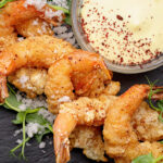Fried shrimp in batter with sauce, on black slate.