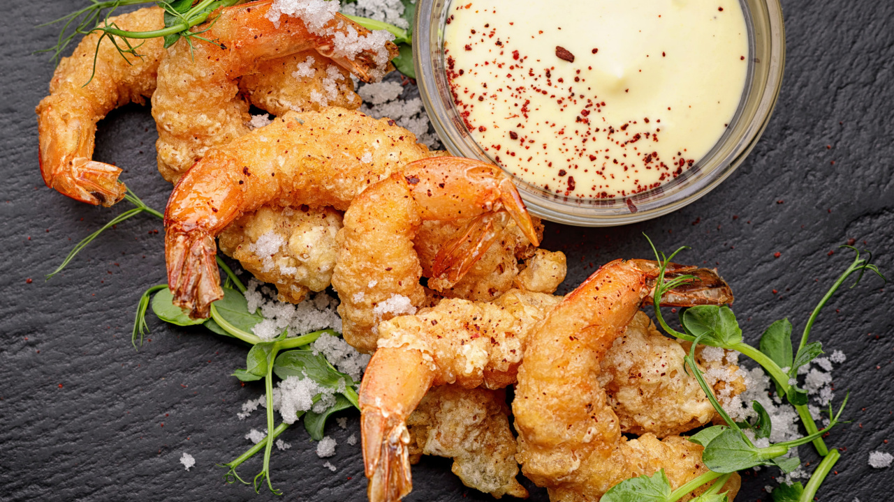 Fried shrimp in batter with sauce, on black slate.
