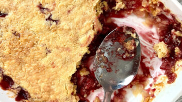 Old fashioned dump cake in a white baking dish with serving spoon.