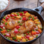 Chicken Afritada. Braised Chicken in Tomato Sauce mixed with potatoes, carrots, bell pepper, and green peas served in frying pan with bowl of cooked rice.