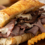French dip sandwich and french fries with bowl of au jus in background on a wooden platter