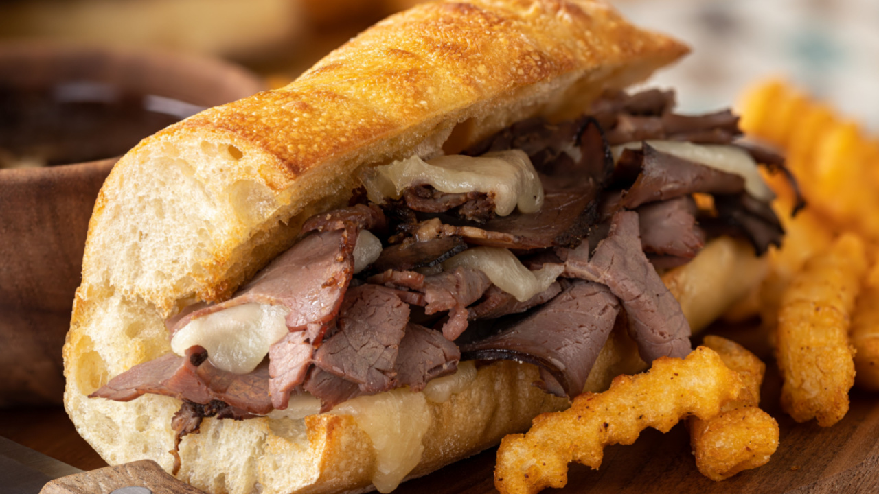 French dip sandwich and french fries with bowl of au jus in background on a wooden platter