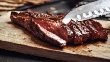 Cutting in slices flank steak on wooden cutting board