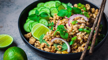 Thai chicken salad larb gai with onion, cucumber and mint in a black plate.