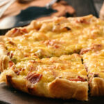 Homemade quiche with leek, ham and cheese on wooden background.
