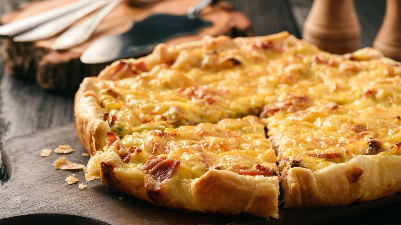 Homemade quiche with leek, ham and cheese on wooden background.