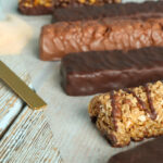 Different tasty bars and scoop of protein powder on wooden table.