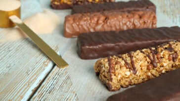 Different tasty bars and scoop of protein powder on wooden table.
