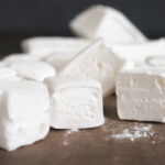 Pile of white homemade marshmallow close-up on wooden cutting board.