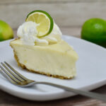 Slice of key lime pie on plate with limes