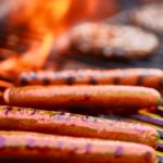tasty hot dogs cooking on grill with hamburgers