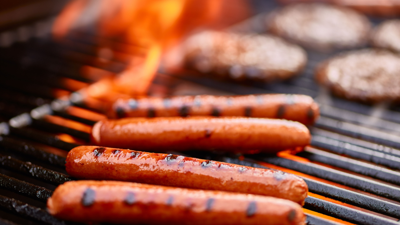tasty hot dogs cooking on grill with hamburgers