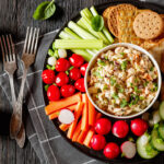 healthy easy leftover salmon salad served with fresh carrots, cucumber, radish, celery, tomatoes and crackers on black plate.