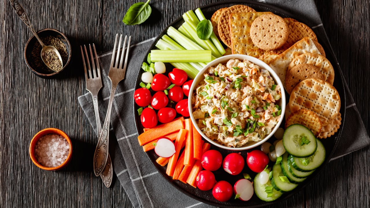 healthy easy leftover salmon salad served with fresh carrots, cucumber, radish, celery, tomatoes and crackers on black plate.
