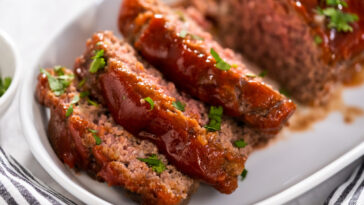 Slicing classic meatloaf with a sweet glaze on a white serving plate