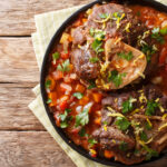 Delicious Italian veal steak Ossobuco alla Milanese with gremolata and vegetable sauce close-up on the table.