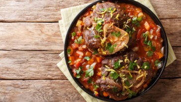 Delicious Italian veal steak Ossobuco alla Milanese with gremolata and vegetable sauce close-up on the table.