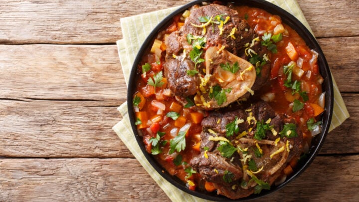 Delicious Italian veal steak Ossobuco alla Milanese with gremolata and vegetable sauce close-up on the table.