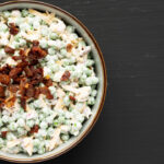 Homemade Creamy Bacon Pea Salad in a Bowl on a black surface, top view. Flat lay, overhead, from above.