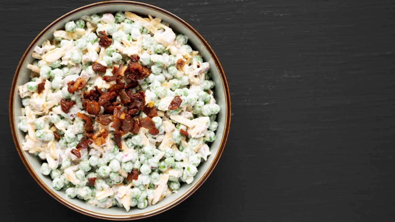 Homemade Creamy Bacon Pea Salad in a Bowl on a black surface, top view. Flat lay, overhead, from above.